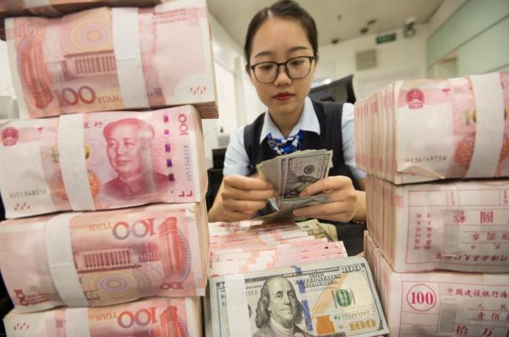 A bank employee counts US currency and Chinese currency notes at a bank on August 6, 2019